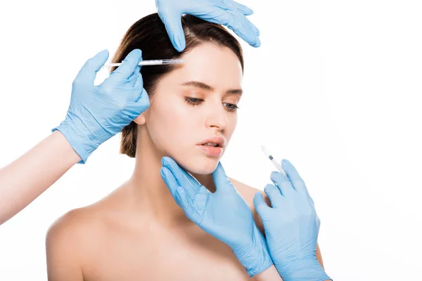 Cropped view of cosmetologists in blue latex gloves touching face of girl while holding  syringes isolated on white — Stock Photo