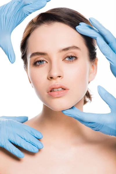 Обрізаний вид пластичних хірургів у синіх латексних рукавичках, що торкаються обличчя дівчини ізольовано на білому — стокове фото