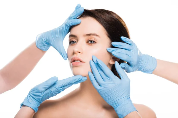 Vista recortada de cirujanos plásticos en guantes de látex azul tocando la cara de mujer desnuda aislada en blanco - foto de stock