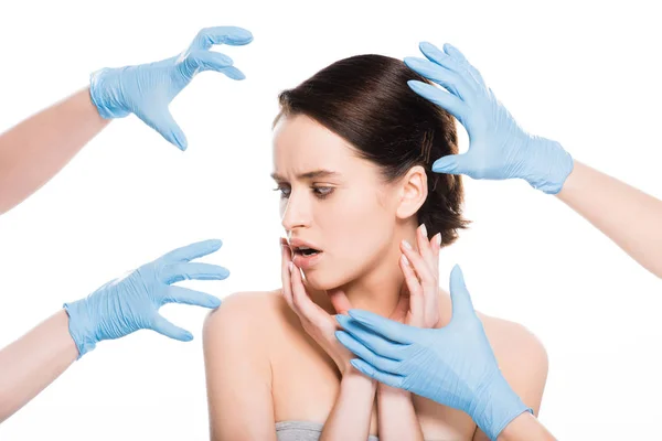 Обрізаний вид пластичних хірургів у синіх латексних рукавичках біля обличчя шокованої дівчини ізольовано на білому — стокове фото