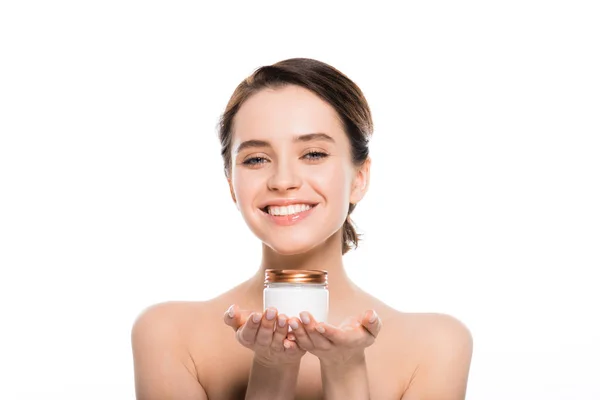 Hübsche und nackte junge Frau hält Container mit Gesichtscreme und lächelt isoliert auf weiß — Stockfoto