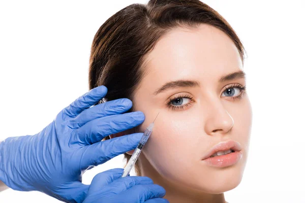 Vue recadrée du cosmétologue en gants de latex bleu tenant la seringue près du visage d'une jeune femme isolée sur du blanc — Photo de stock