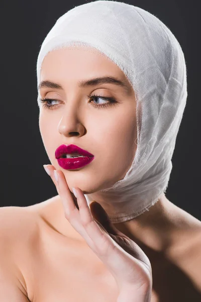 Attraktives Mädchen mit bandagiertem Kopf, das Gesicht isoliert auf grau berührt — Stockfoto