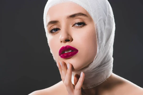 Attractive young woman with bandaged head touching face and looking at camera isolated on grey — Stock Photo