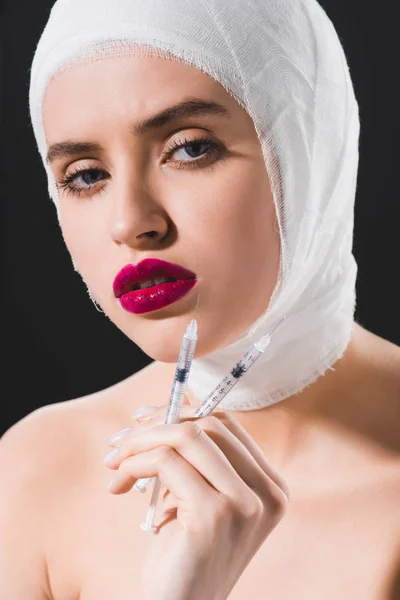 Attraktive junge Frau mit bandagiertem Kopf und Spritzen isoliert auf grau — Stockfoto