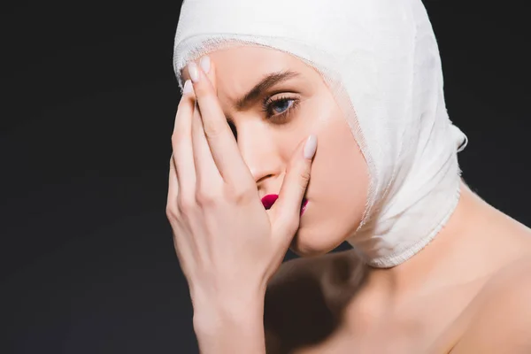 Jeune femme avec tête pansée couvrant le visage isolé sur gris — Photo de stock