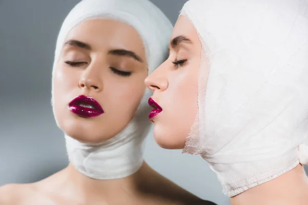 Spiegelbild einer attraktiven jungen Frau mit bandagiertem Kopf und geschlossenen Augen auf grau — Stockfoto