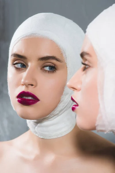 Mirror reflection of young pretty woman with bandaged head on grey — Stock Photo