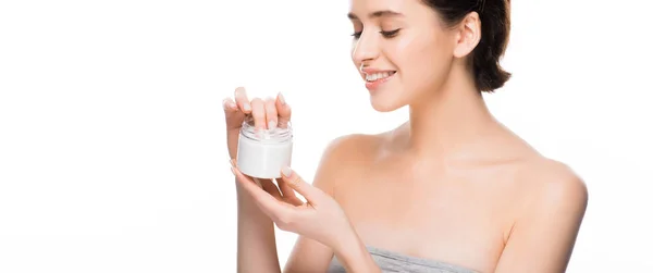 Plano panorámico de mujer alegre mirando contenedor con crema facial y sonriendo aislado en blanco - foto de stock