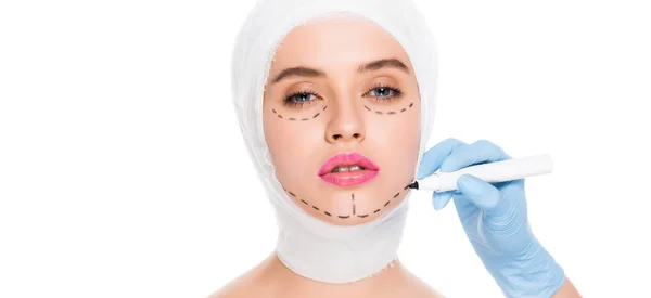 Colpo panoramico di chirurgo plastico in guanto di lattice che tiene pennarello vicino alla donna con segni sul viso isolato su bianco — Foto stock