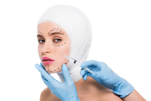 Vista recortada del cirujano plástico en guantes de látex azul que sostiene la jeringa cerca de la cara de la mujer con marcas aisladas en blanco - foto de stock