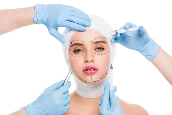 Visão recortada de cirurgiões plásticos em luvas de látex azul com equipamentos médicos perto da face da mulher com marcas isoladas em branco — Fotografia de Stock