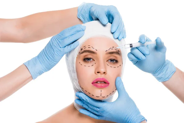 Cropped view of plastic surgeons in blue latex gloves with syringe near face of woman with marks isolated on white — Stock Photo