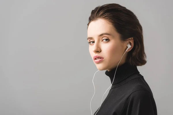 Молодая женщина в черном джампере слушает музыку в наушниках, изолированных на сером — стоковое фото