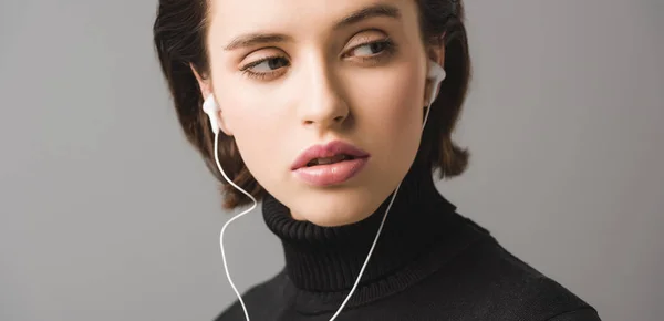 Panoramic shot of woman in black jumper listening music in earphones isolated on grey — Stock Photo