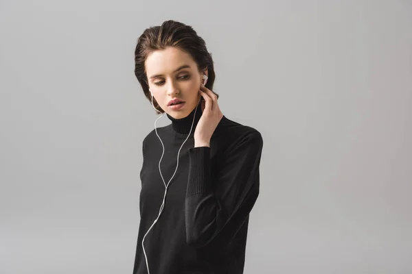 Jolie fille en pull noir écouter de la musique dans des écouteurs isolés sur gris — Photo de stock