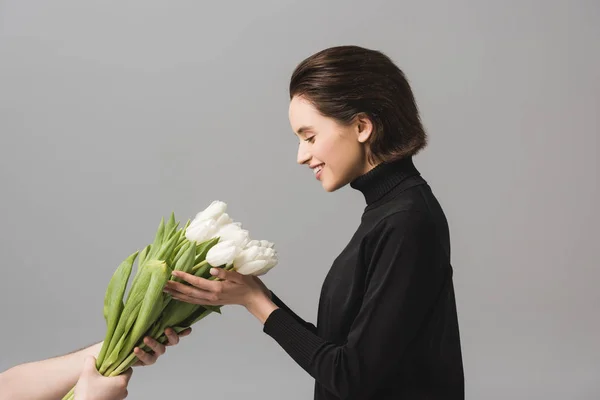 Cropped view of man holding white tulips near smiling woman isolated on grey — Stock Photo
