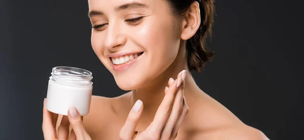 Plano panorámico de mujer alegre sosteniendo contenedor con crema facial y sonriendo aislado en gris - foto de stock