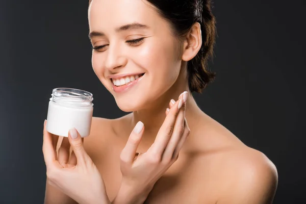 Cheerful woman holding container with face cream and smiling isolated on grey — Stock Photo