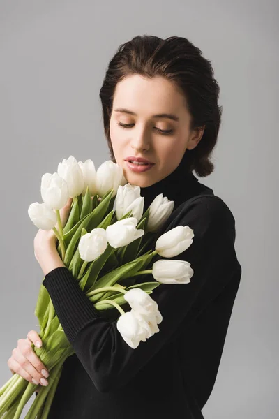Mulher morena atraente olhando para tulipas brancas isoladas em cinza — Fotografia de Stock