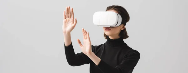 Plano panorámico de la joven morena con auriculares de realidad virtual mientras gesticulaba aislado en gris — Stock Photo