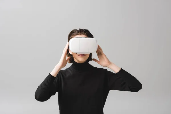 Молода жінка торкається гарнітури віртуальної реальності ізольовані на сірому — стокове фото