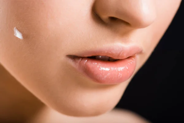 Vista recortada de la mujer con crema cosmética en la cara aislada en negro - foto de stock