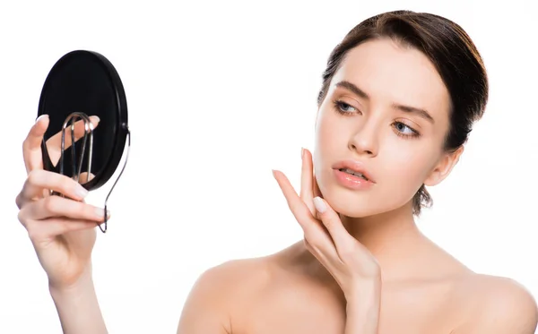 Jeune femme brune touchant le visage et regardant miroir isolé sur blanc — Photo de stock
