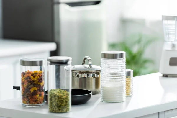 Recipientes de vidro com cereais perto de frigideira e panela na cozinha — Fotografia de Stock