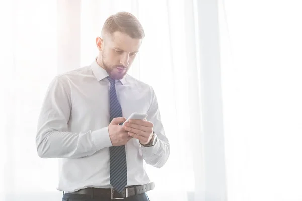 Schöner bärtiger Mann im Anzug benutzt Smartphone, während er zu Hause steht — Stockfoto