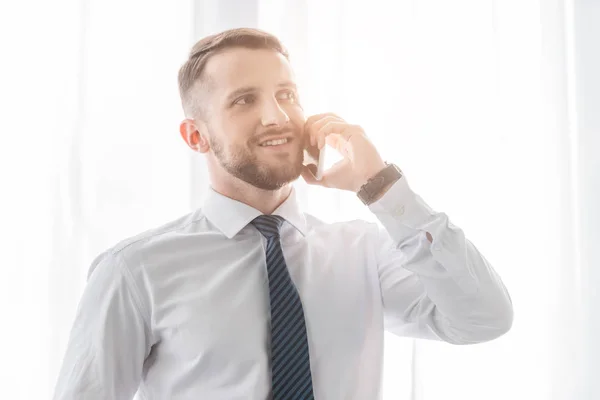 Hombre barbudo alegre hablando en el teléfono inteligente y sonriendo en casa — Stock Photo