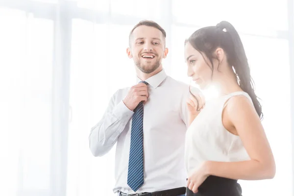 Весёлый мужчина трогает галстук и смотрит на привлекательную женщину — стоковое фото