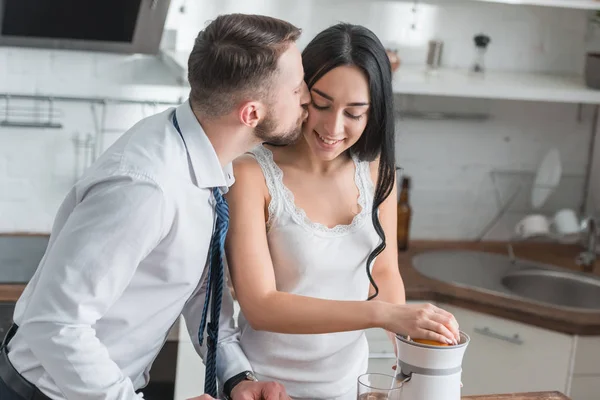 Handsome bearded man kissing cheek of happy brunette girl in kitchen — Stock Photo