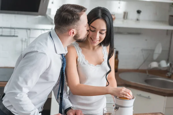 Guapo barbudo hombre besar mejilla de feliz morena chica en cocina - foto de stock