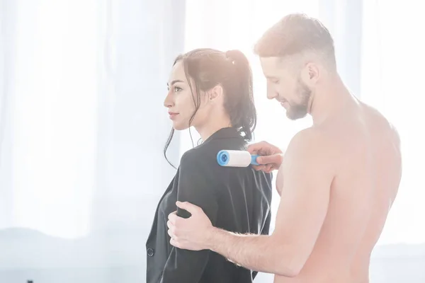 Bearded muscular man cleaning formal wear of woman with lint roller — Stock Photo