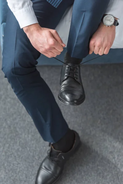 Vista recortada del hombre atando cordones de zapatos en zapatos negros en casa - foto de stock