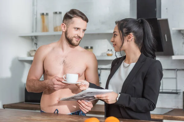 Fröhlicher, hemdloser Mann mit Tasse Kaffee in der Nähe attraktiver Brünetten mit Zeitung — Stockfoto