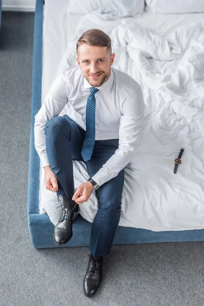 Vista superior del hombre alegre en ropa formal atando cordones en la cama - foto de stock