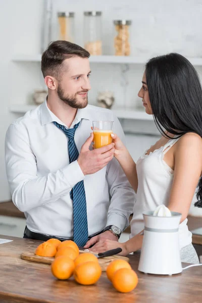 Mulher morena atraente dando vidro de suco de laranja fresco para o homem de terno — Fotografia de Stock