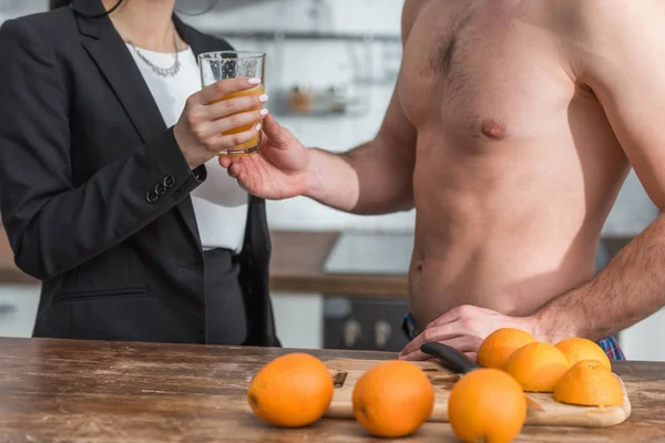 Vista recortada de hombre musculoso dando vaso de jugo de naranja fresco a chica - foto de stock