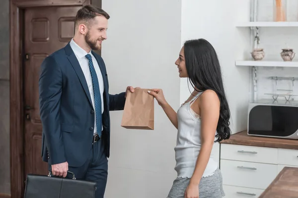 Joyeuse jeune femme donnant sac en papier à l'homme avec mallette — Photo de stock