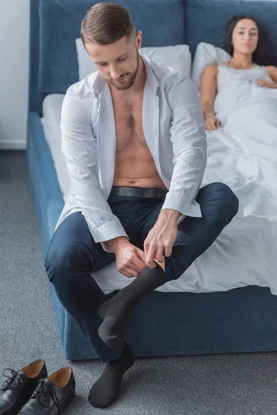 Enfoque selectivo del hombre barbudo en traje con calcetines mientras está sentado en la cama cerca de la mujer - foto de stock