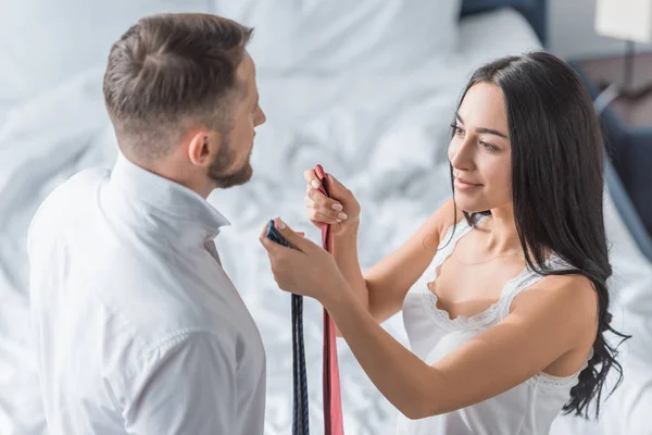 Overhead view of cheerful brunette woman holding ties in hands near bearded man — Stock Photo