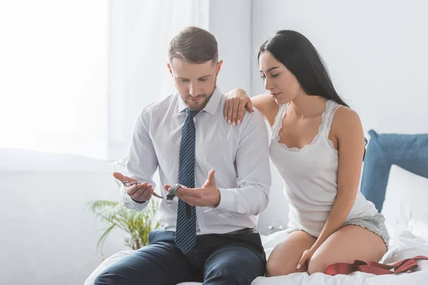 Attractive brunette woman sitting near handsome boyfriend looking at watch in bedroom — Stock Photo