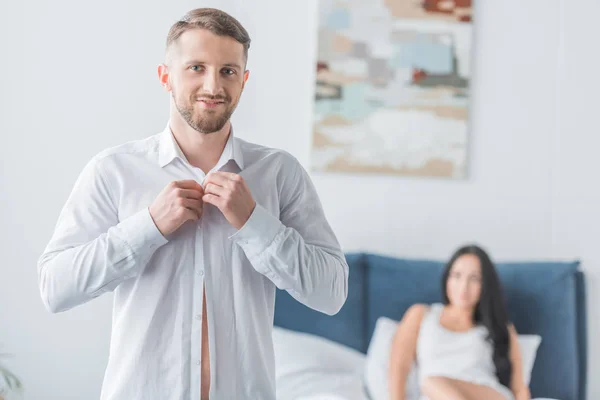 Cheerful bearded man wearing shirt and looking at camera near woman in bed — Stock Photo
