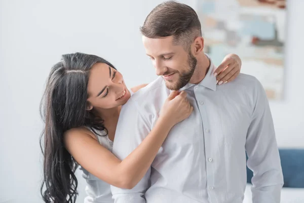 Feliz joven mujer tocando collares de alegre novio en camisa blanca - foto de stock