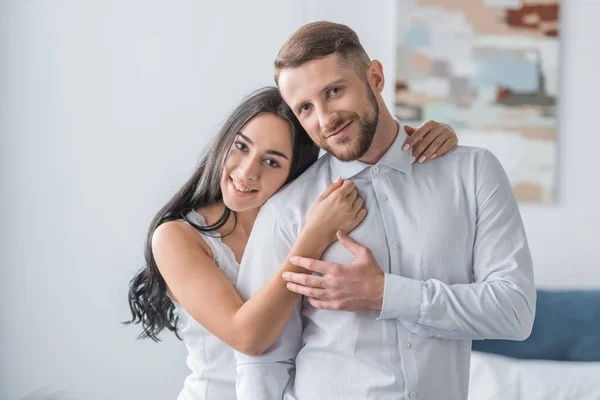 Feliz joven mujer abrazando alegre novio en blanco camisa - foto de stock