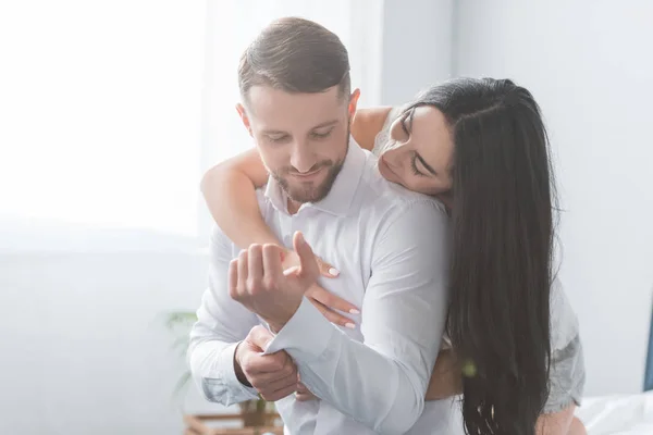 Allegra fidanzata abbracciare fidanzato barbuto in camicia bianca a casa — Foto stock