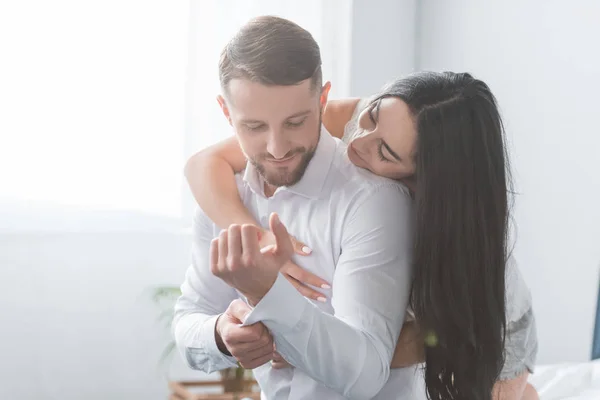 Petite amie gaie étreignant petit ami barbu en chemise blanche à la maison — Photo de stock