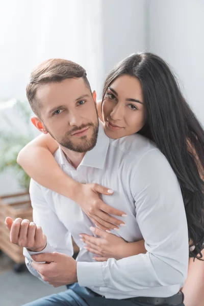 Feliz namorada abraçando namorado barbudo em camisa branca em casa — Fotografia de Stock
